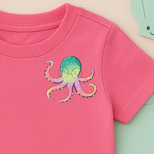Könnte beinhalten: Ein pinkfarbenes T-Shirt mit Rundhalsausschnitt und einem farbenfrohen Oktopus-Motiv mit Brille. Der Oktopus hat einen blau-grünen Kopf und gelbe und violette Tentakel. Eine blaue Jeans-Shorts und ein hellgrünes T-Shirt sind sichtbar.