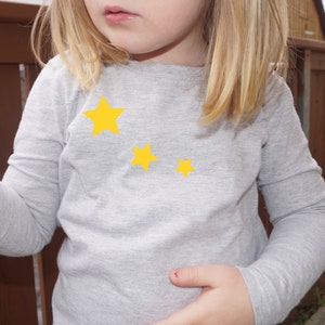 Könnte beinhalten: Ein graues Langarmshirt mit drei gelben Sternen auf der Vorderseite.