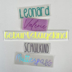 Könnte beinhalten: Fünf rechteckige Klebeetiketten mit individuellem Text. Das oberste Etikett zeigt den Namen Leonard in türkisfarbenem Glitzer. Darunter befindet sich ein lilafarbenes Etikett mit dem Namen Valerie. Ein langes gelbes Etikett trägt die Aufschrift Geburtstagskind. Ein weißes Etikett zeigt SCHULKIND. Das untere Etikett ist irisierend und trägt das Wort Mutterpass.