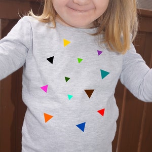 Può includere: Una maglietta grigia a maniche lunghe con una varietà di forme triangolari colorate stampate sul davanti.