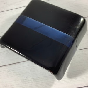 May include: A black square-shaped box with a blue stripe across the top. The box is made of a glossy material.