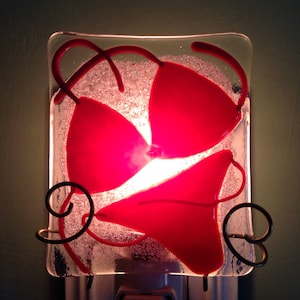 May include: A red glass nightlight shaped like a bikini top. The light is on and the glass is illuminated with a warm glow.