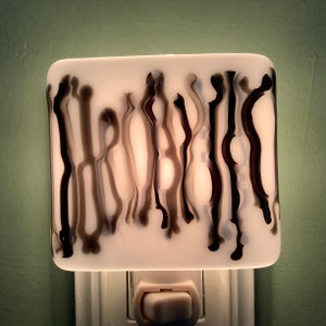 May include: A white night light with a black and gray wavy pattern. The light is plugged into an outlet and has a switch.