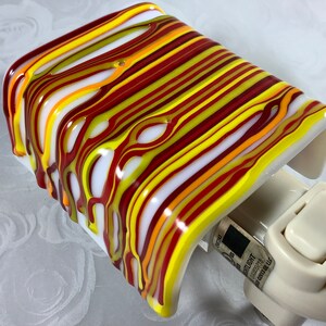 May include: A white night light with a red, yellow, and orange striped glass shade. The shade has a melted, dripping effect. The night light has a white switch.