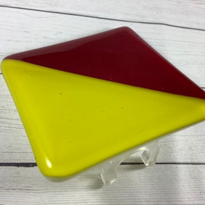 May include: A square glass coaster with a diagonal line dividing it into two sections. The top section is a deep red color, and the bottom section is a bright yellow color.