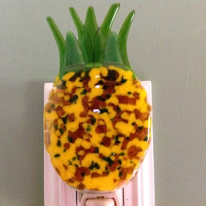 May include: A yellow and green glass pineapple night light plug-in. The pineapple is made of glass with a textured surface and has a green leafy top.