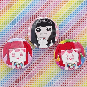 May include: Three colorful round buttons with anime-style illustrations. One button features a girl with black hair and a tiara on a pink background. The other two buttons have a girl with red hair and a sign.