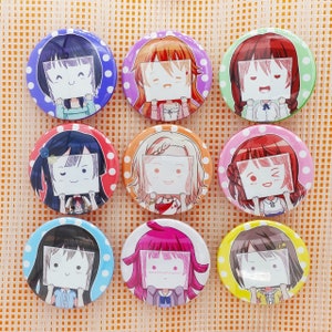 Puede incluir: Nueve botones redondos con ilustraciones de estilo anime de chicas sosteniendo carteles en blanco. Cada botón presenta una chica diferente con varios colores de pelo y atuendos, sobre un fondo de lunares en colores como azul, rosa y amarillo.