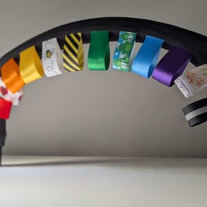 May include: A black stroller bar with a rainbow of colorful ribbons attached. The ribbons have different patterns, including bees, frogs, and stripes.