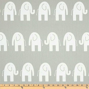 May include: A fabric with a repeating pattern of white elephant silhouettes on a light gray background. The elephants are stylized with rounded bodies, trunks, and ears. The fabric is likely used for home decor or children's items.