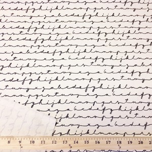 May include: A white fabric with a black repeating pattern of handwritten letters of the alphabet. A ruler is visible at the bottom of the image.