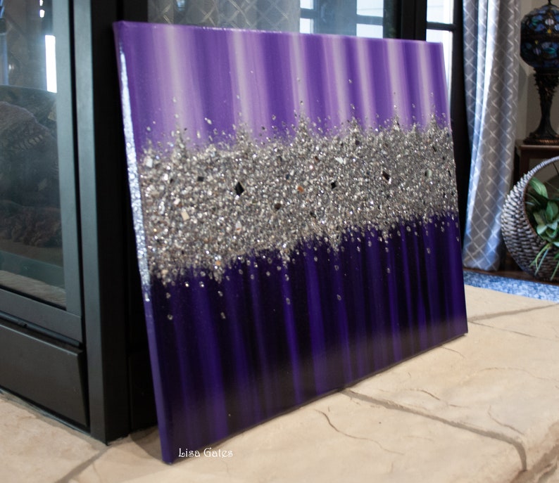 May include: Purple and silver abstract painting with a textured glitter design. The painting is on a canvas and has a white border. The artist's signature, "Lisa Gates", is in the lower right corner.