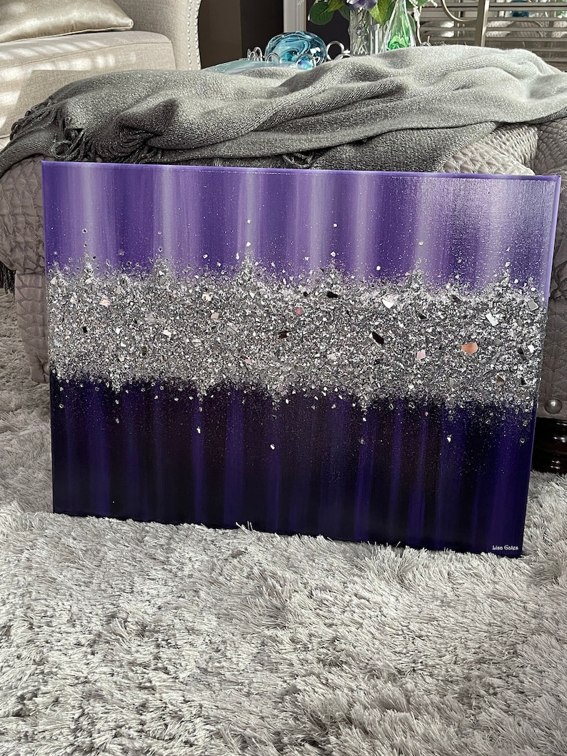 May include: Purple and silver abstract painting with a textured glitter finish. The painting is on a canvas and has a white border. The artist's signature is in the bottom right corner.