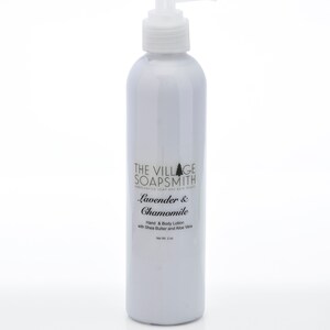 K&ouml;nnte beinhalten: Eine wei&szlig;e Flasche mit Lavendel- & Kamillen-Hand- und K&ouml;rperlotion mit einem Pumpspender. Die Flasche ist mit "The Village Soapsmith" beschriftet und hat ein Nettogewicht von 2 oz.