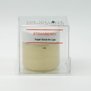 May include: A clear plastic container with a white jar inside. The jar is labeled "Strawberry Sugar Scrub for Lips" and "1 oz".