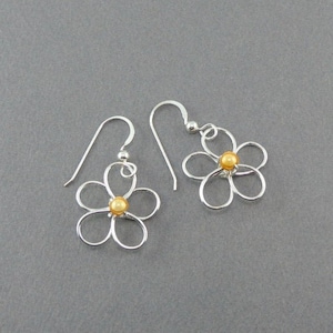 May include: Silver dangle earrings with a delicate flower design and a gold bead in the center.