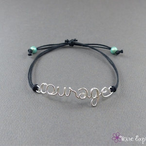 May include: A black string bracelet with turquoise beads and a silver wire word charm that says "courage".