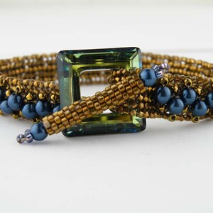 May include: A gold and blue beaded bracelet with a green square-shaped clasp.