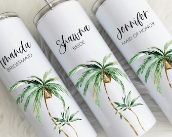 May include: Three white stainless steel tumblers with straws and palm tree designs. The tumblers are personalized with the names "Amanda Bridesmaid", "Shawna Bride", and "Jennifer Maid of Honor".