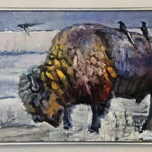 May include: An oil painting in a silver frame depicting a large bison with thick, textured fur in shades of brown, yellow, and red. Two black birds perch on the bison's back, while another flies in a snowy, pale blue landscape with visible brushstrokes.