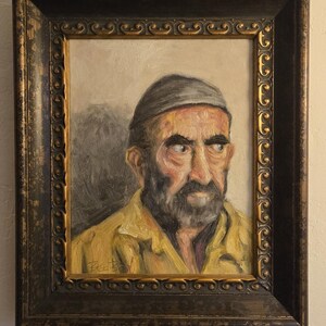 May include: A framed oil painting of a man with a beard wearing a yellow jacket and a gray hat. The man is looking to the right of the frame.