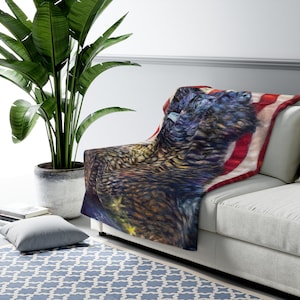 May include: A soft, plush throw blanket featuring a stylized American bald eagle with a starry background and red, white, and blue stripes. The eagle is depicted with its wings spread wide, as if in flight.
