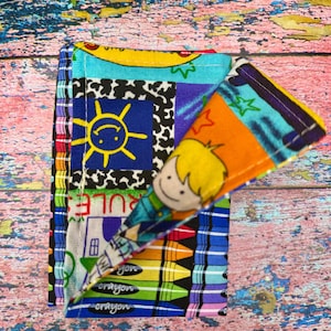 Könnte beinhalten: Eine bunte Patchwork-Stoffbrieftasche mit einem Buntstift-Design. Die Brieftasche zeigt eine lächelnde Sonne, einen Cartoon-Jungen und das Wort "RULE". Das Design umfasst eine Vielzahl von Farben, darunter Blau, Gelb, Orange und Grün.
