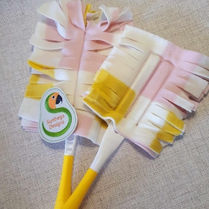 May include: Two yellow and white duster heads with pink and yellow fringe. The duster heads are attached to yellow handles with white tips. A green and yellow logo with the text "Sunthaega Designs" and a parrot illustration is visible.