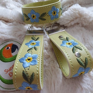 Puede incluir: Dos llaveros de cuero verde con anillas de plata y bordado de flores azules de nomeolvides. Un llavero es de estilo pulsera sin anilla.