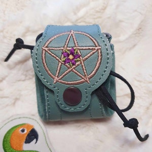 May include: A small teal leather pouch with a drawstring closure. The pouch has a pentagram embroidered on the front with a pink flower in the center.