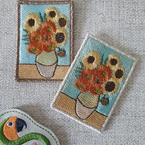 Könnte beinhalten: Zwei gestickte Aufnäher mit einem Strauß Sonnenblumen in einer Vase. Die Aufnäher befinden sich auf einem hellbeigen Stoffhintergrund. Die Aufnäher sind braun, gelb, orange und grün.
