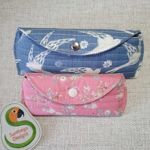 May include: Two fabric eyeglass cases, one blue with a white bird pattern and one pink with a floral pattern. Both cases have a button closure.