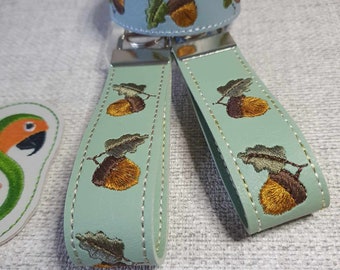 Puede incluir: Dos llaveros de cuero verde claro con un llavero plateado y diseños de bellotas bordadas. También se incluye una pulsera de cuero azul claro con un diseño de bellota bordada.