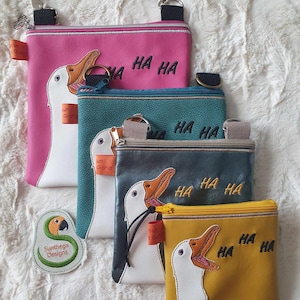 May include: Four different sized zippered pouches with a white goose design and the text "HA HA" embroidered on them. The pouches are in pink, teal, gray, and yellow.