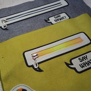 May include: Close-up of two fabric pouches. One is gray with a white zipper and the text "SAY WHAT?" in a speech bubble. The other is yellow with a gradient zipper and a parrot patch.