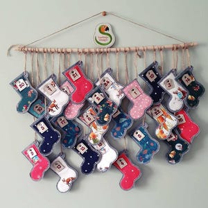 May include: A Christmas advent calendar with 24 fabric stockings hanging from a wooden dowel. Each stocking is decorated with a different pattern and has a number from 1 to 24 sewn on it.