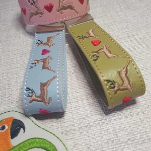 May include: Two leather keychains with embroidered reindeer and hearts. One keychain is light blue and the other is olive green.