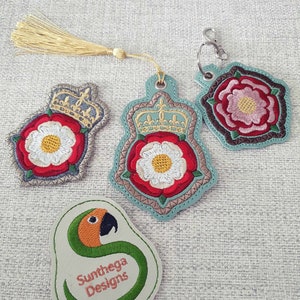 May include: Three embroidered patches featuring a white rose with a crown and a green snake with the text "Sunthega Designs".
