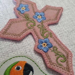 May include: A pink leather cross with a silver chain and embroidered forget-me-not flowers.