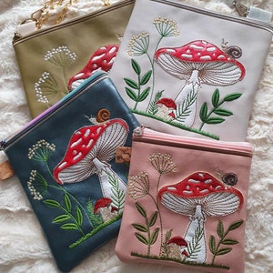 Pode incluir: Quatro pequenas bolsas crossbody quadradas em verde oliva, creme, verde-azulado e rosa. Cada bolsa apresenta um design bordado de um cogumelo vermelho e branco, folhas verdes e um caracol. As bolsas têm alças de corrente e fechos de zíper.