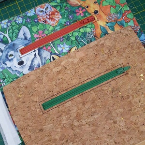 May include: A cork fabric pouch with a green zipper. The pouch is on a green cutting mat. The fabric is printed with a woodland scene with a wolf, deer, owl, and flowers.