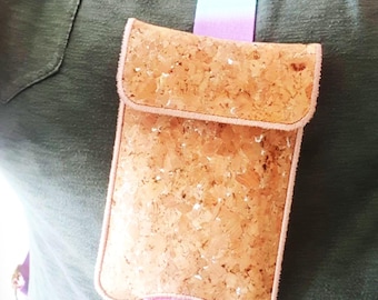 May include: A cork crossbody bag with a flap closure and a pink trim. The bag is suspended by a colorful strap with a gold-colored clasp. The bag is worn over a green shirt.