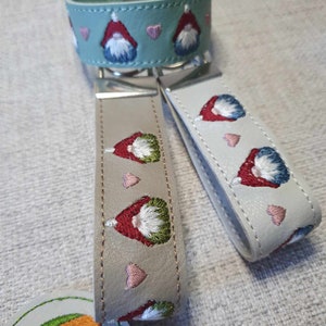 May include: Two leather keychains with embroidered gnomes and hearts. One keychain is light blue and the other is beige.