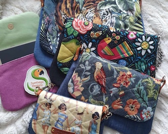 Può includere: Cinque piccole borse di jeans con diversi motivi colorati. Le borse hanno una chiusura a lembo e una tracolla a catena dorata. I motivi includono tigre, uccelli, fiori e donne in costume da bagno.