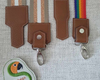 May include: Three different camera straps with brown leather accents and silver swivel clips. The straps are made of woven fabric with different patterns: beige with white stripes, rainbow stripes, and beige with gold stripes. The straps are labeled with the text "Sunthaga Designs".
