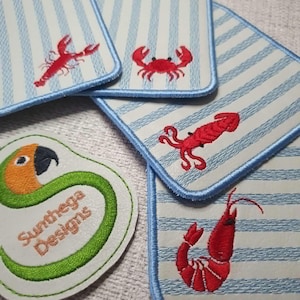 May include: A collection of rectangular fabric patches featuring light blue and white stripes with embroidered red sea creatures including a lobster, crab, squid, and shrimp, alongside a circular patch with a parrot and the text Sunthega Designs.