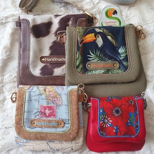 Könnte beinhalten: Vier verschiedene handgefertigte Umhängetaschen mit verschiedenen Mustern und Farben. Die Taschen sind aus Leder und Stoff und haben einen Klappverschluss mit einer Metallschnalle. Jede Tasche hat ein kleines Metallschild mit der Aufschrift "Handmade".
