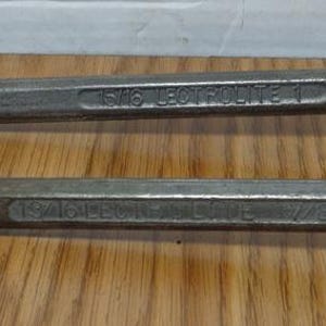 May include: Two vintage, steel wrenches with open-ended heads. The wrenches are silver-colored and lie on a wooden surface. The tools are designed for tightening or loosening nuts and bolts.