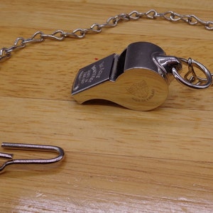 May include: A silver whistle with a chain attached. The whistle has the words "The Acme Whistle" and "Made in England" engraved on it.