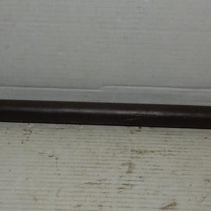 May include: A large, dark brown wrench with a circular head and a long, tapered handle. The wrench appears to be made of metal and is designed for heavy-duty use. The head has a large opening, and the handle extends to a pointed end.